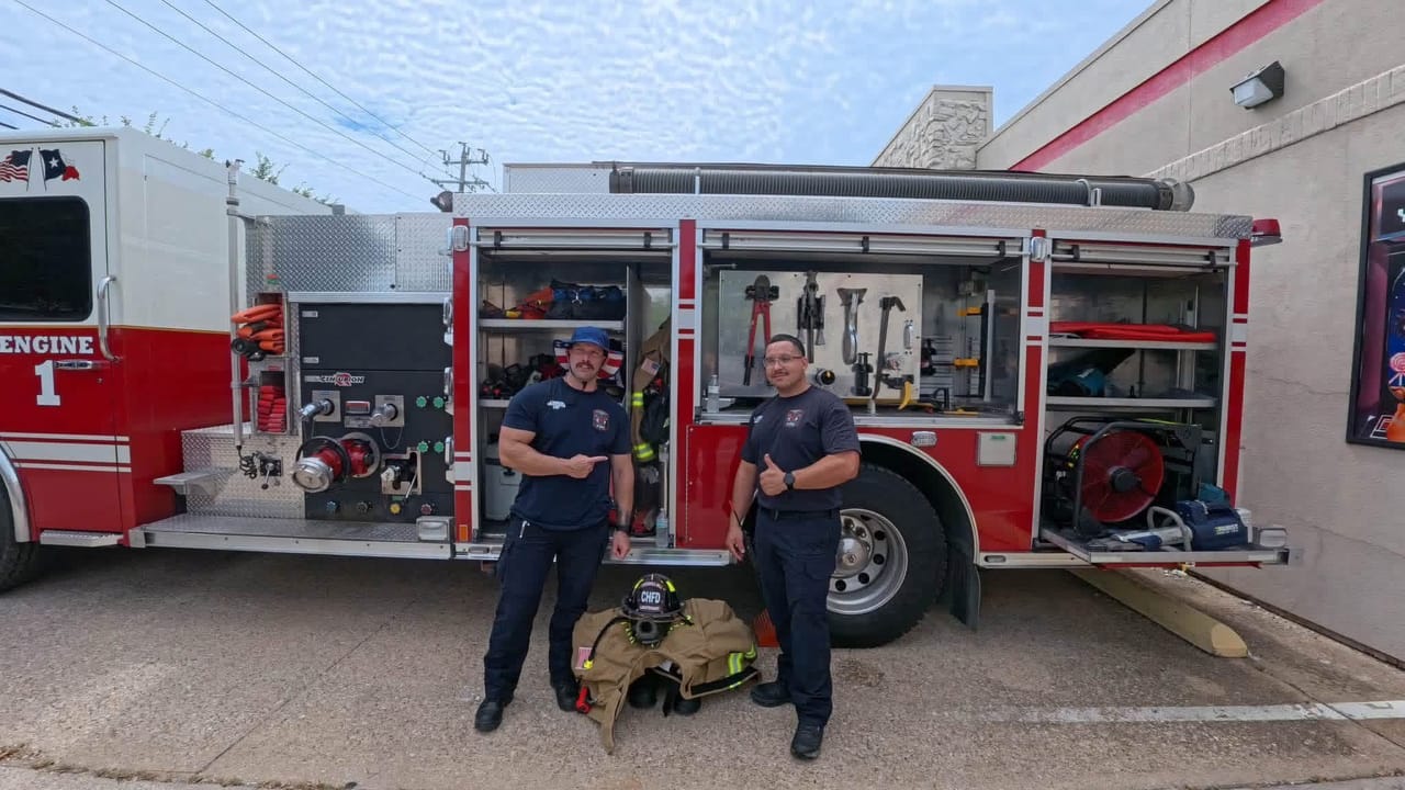 Two firefighters stand beside Engine 1 with its equipment compartments open, showing tools and hose