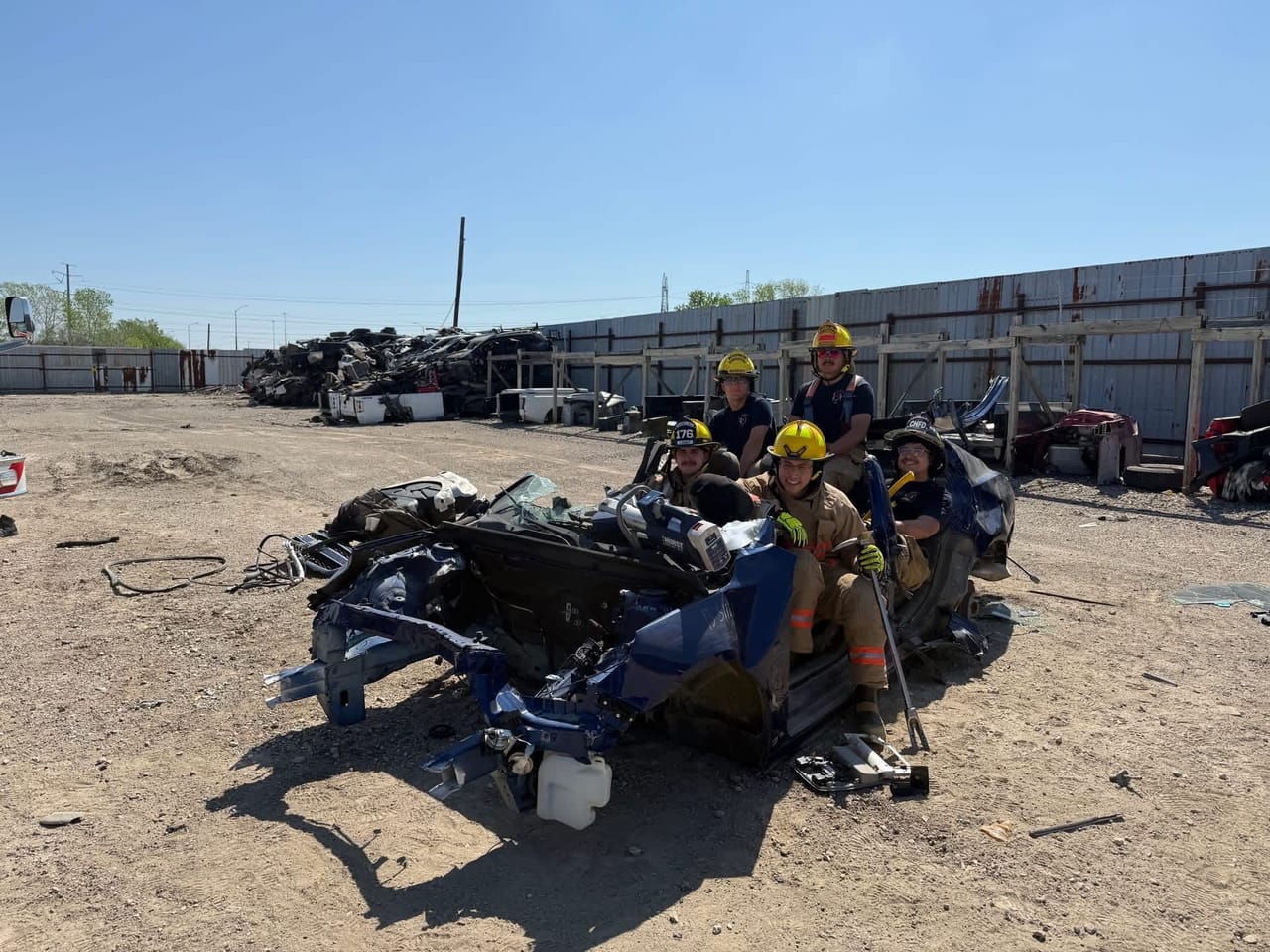 Firefighters in helmets and turnout gear practice cutting apart a wrecked car during rescue training