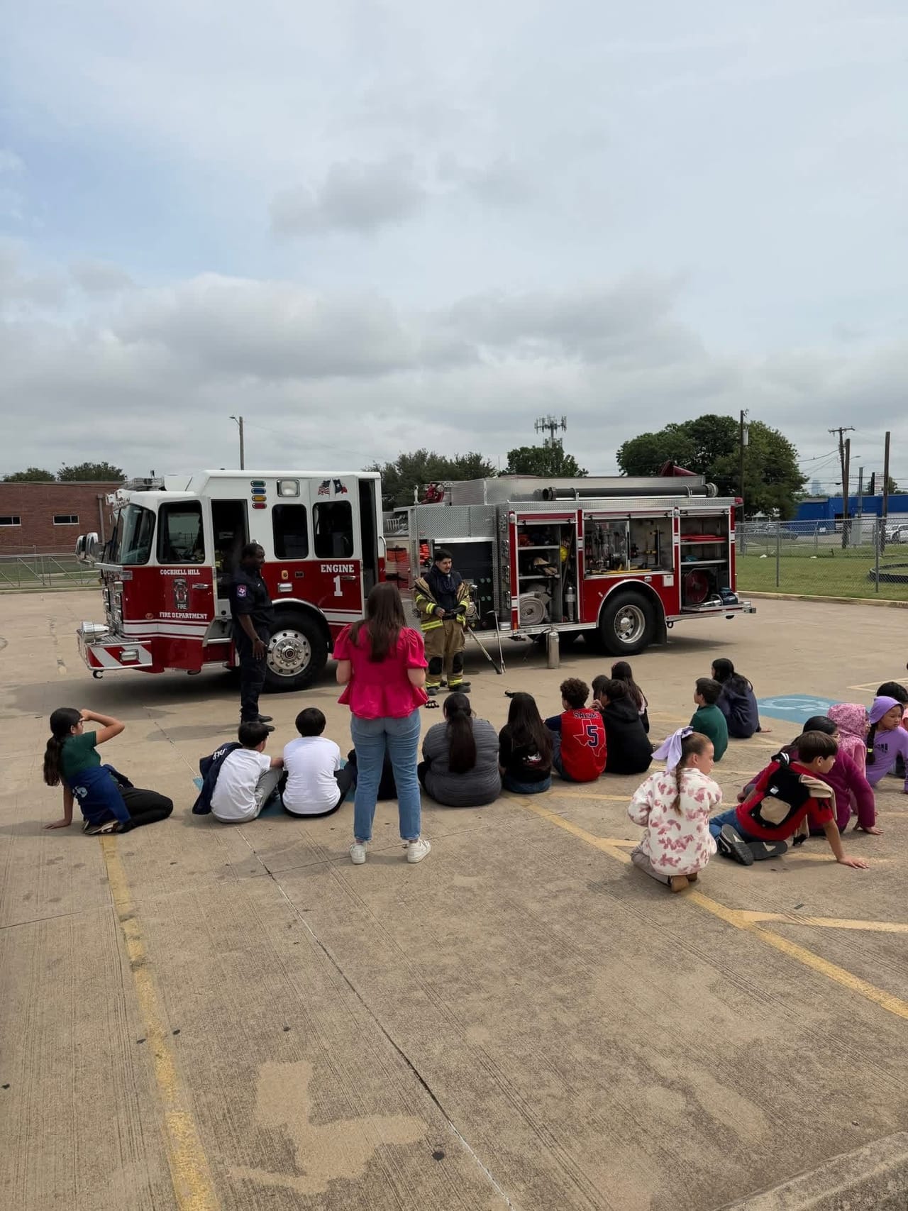Schoolchildren sit on the pavement facing Engine 1 and a second fire engine during a school visit
